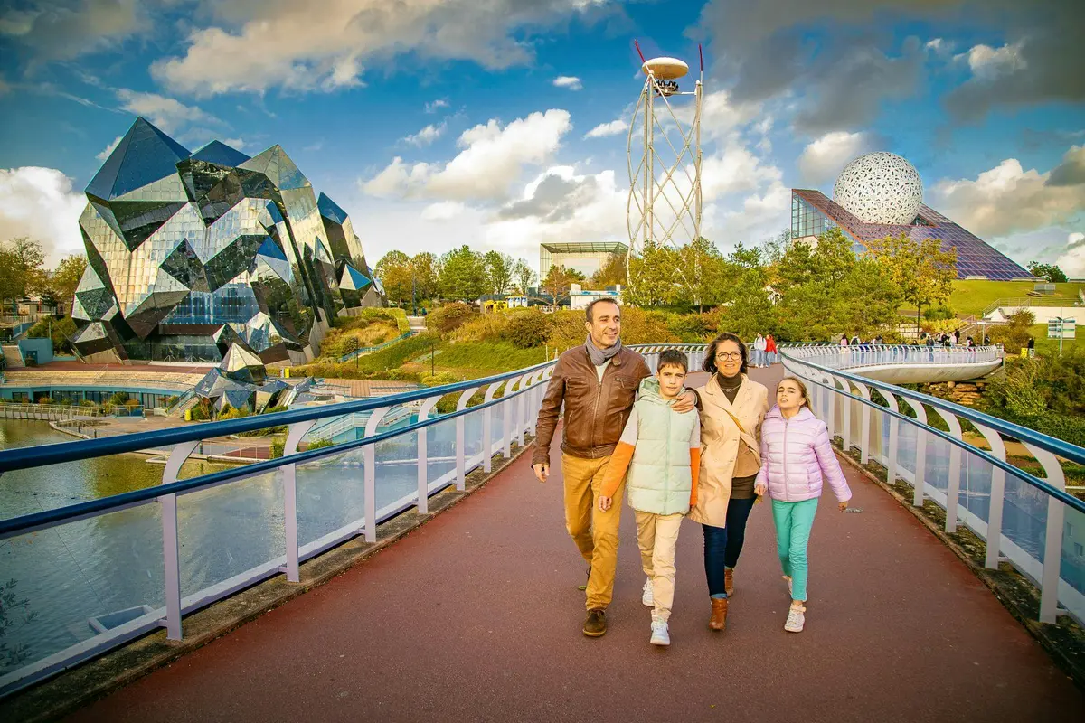 Une famille de quatre personnes marchant sur un large chemin avec, en arrière-plan, un parc futuriste composé de dômes et de tours.