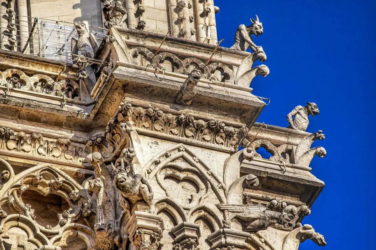 Des gargouilles en pierre détaillées ornent une cathédrale gothique sur fond de ciel bleu clair.