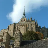 Grand château de pierre avec flèches et tourelles, entouré d'arbres, vu d'en bas avec les toits au premier plan. Ciel bleu avec des nuages au-dessus. &copy; Bluetrain