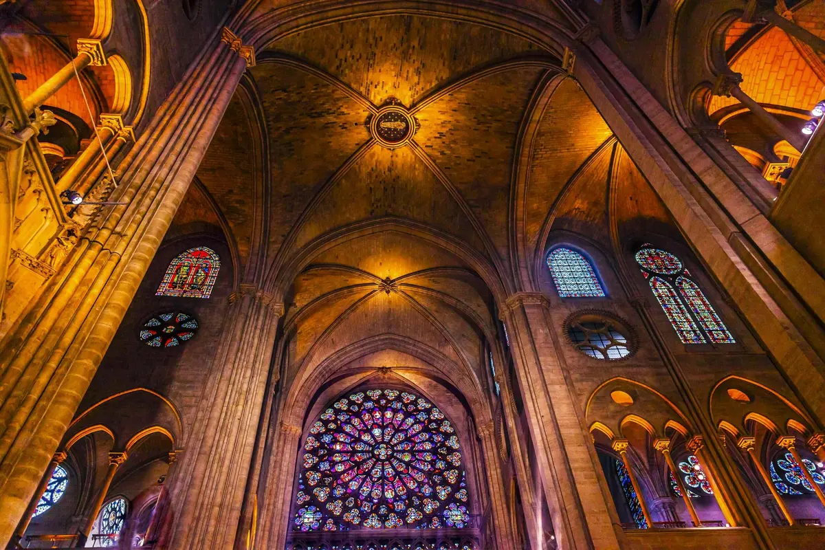 Vue de l'intérieur d'une cathédrale, mettant en évidence son haut plafond voûté, ses vitraux ornés et une grande rosace.