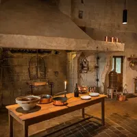Une cuisine rustique, à l'ancienne, avec une grande cheminée en pierre, une table en bois, des casseroles en cuivre et divers ustensiles de cuisine. &copy; Léonard de Serres