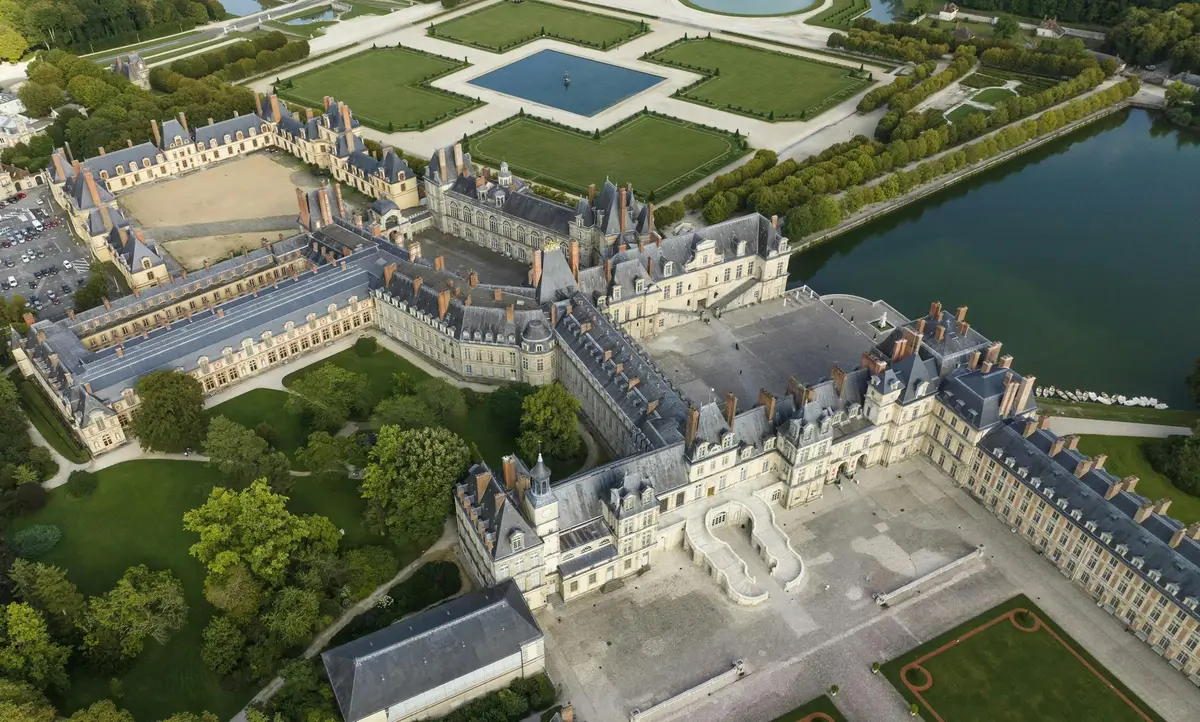 Aerial view of an ornate historical chateau with extensive gardens and symmetrical water features.