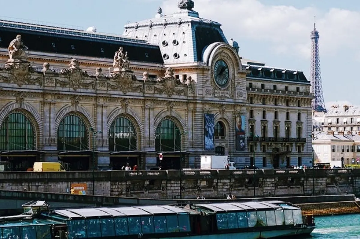 Bâtiment historique avec une grande horloge sur la façade, des détails ornementaux et des fenêtres cintrées. Un bateau est visible au premier plan.