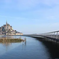 Un pont incurvé mène à une île historique dotée d'une structure haute et pointue, entourée d'une eau calme sous un ciel bleu clair. &copy; Mathias Neveling