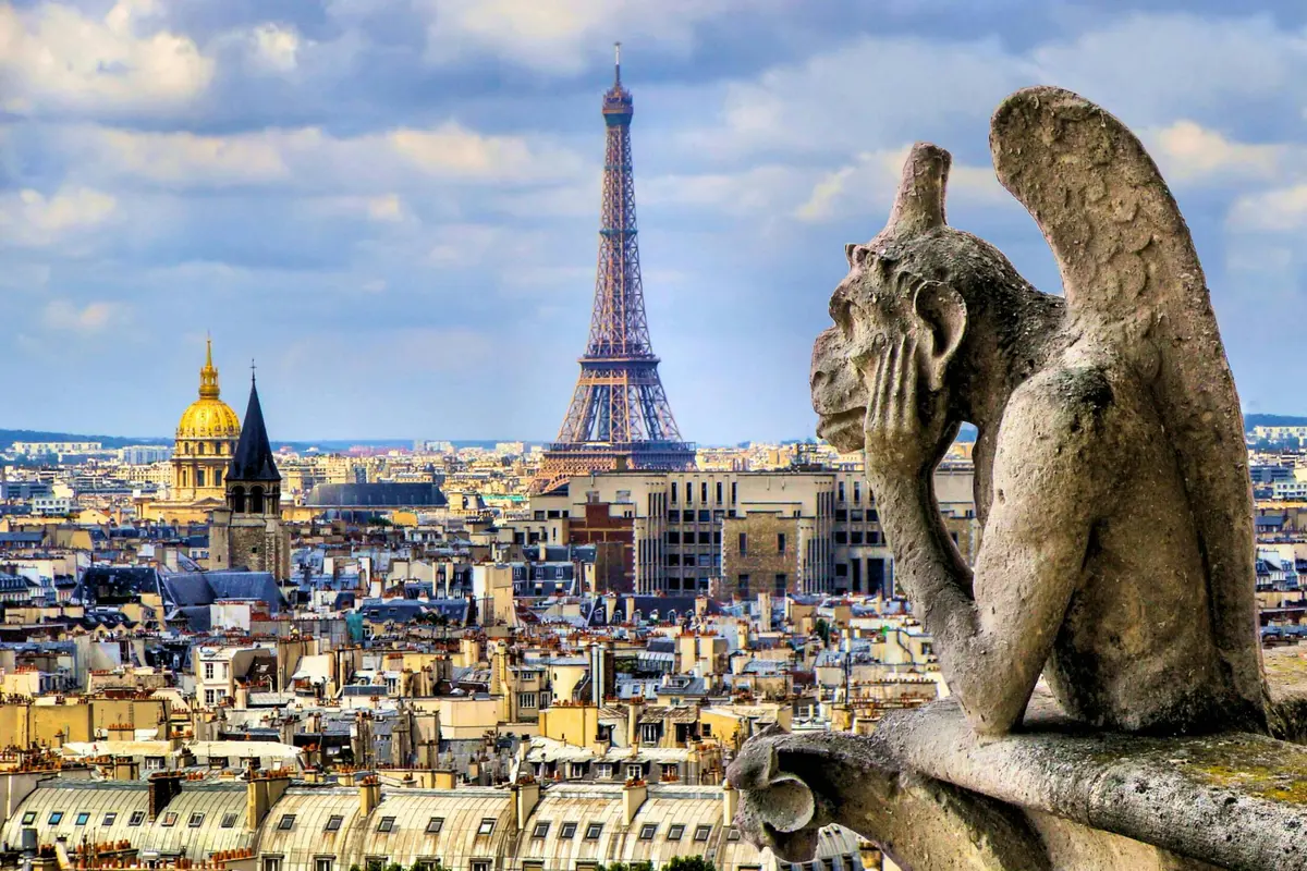 Une gargouille en pierre surplombe Paris avec la Tour Eiffel en arrière-plan sous un ciel partiellement nuageux.