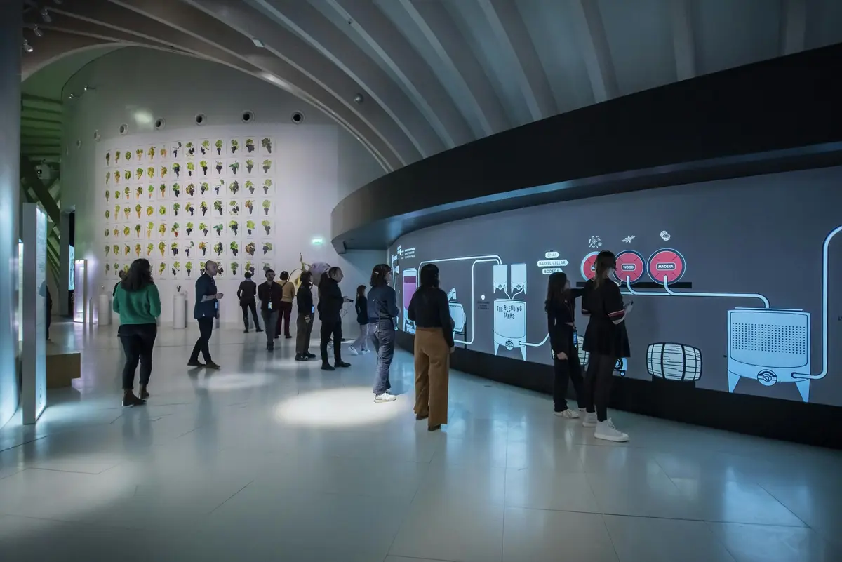 Des personnes interagissent avec un grand écran numérique incurvé dans une pièce moderne et spacieuse aux murs blancs et aux installations artistiques.