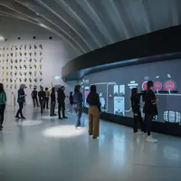 Des personnes interagissent avec un grand écran numérique incurvé dans une pièce moderne et spacieuse aux murs blancs et aux installations artistiques. &copy; Elab®Photo Anaka - Agence Clémence Farrell - Ich&Kar- The Mill