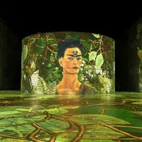 Une installation artistique immersive présentant le portrait d'une femme entourée de verdure luxuriante et de vignes, projeté sur un mur incurvé. &copy; @Culturespaces / Geoffroy Groult