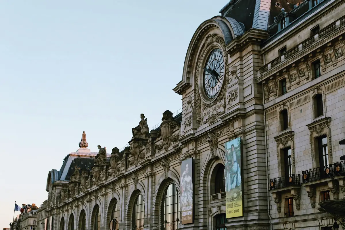 Façade ornée d'un bâtiment historique avec des fenêtres cintrées, des statues et de grandes affiches sous un ciel dégagé.