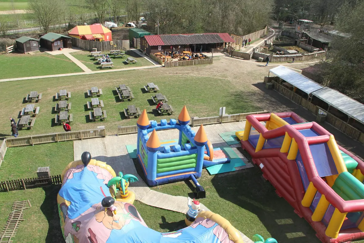 Vue aérienne d'une aire de jeux extérieure avec des structures gonflables, des tables de pique-nique et quelques bâtiments dans un parc.