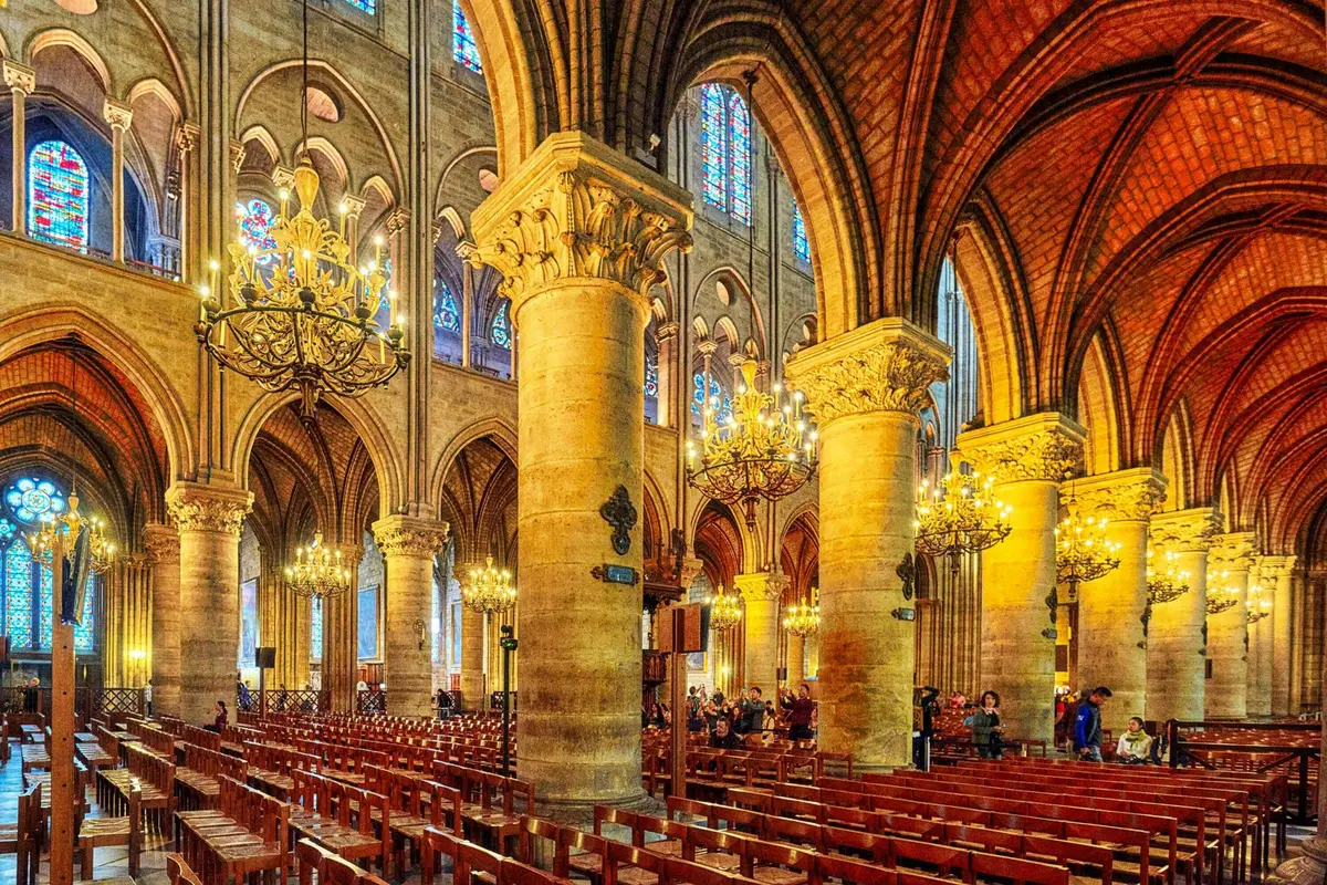 Vue intérieure d'une cathédrale avec de hauts piliers, des plafonds voûtés, des lustres, des vitraux et des bancs en bois.