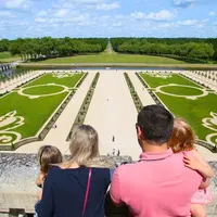 Une famille de quatre personnes contemple des jardins méticuleusement conçus, avec des allées symétriques et des pelouses vertes ornées de motifs décoratifs. &copy; Ludovic Letot