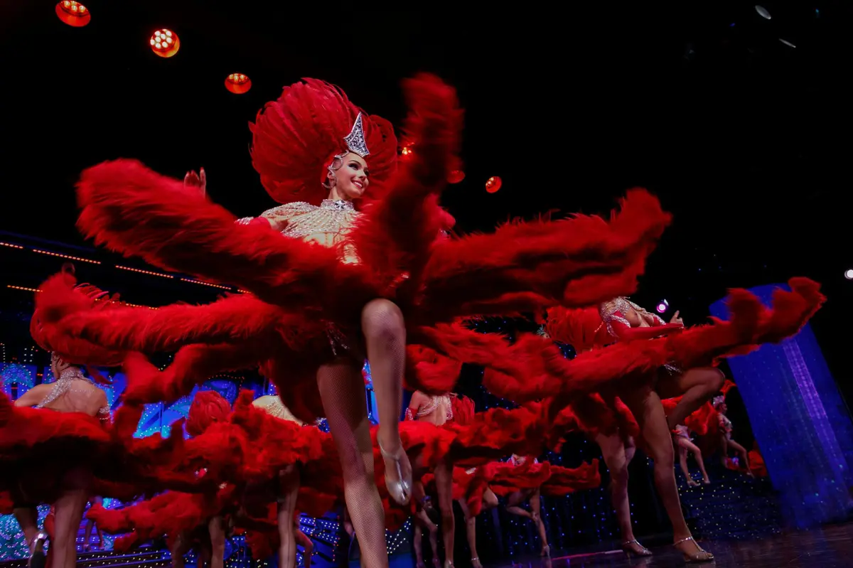 Une artiste vêtue d'un costume rouge orné de plumes très élaboré, qui danse sur scène sous des lumières vives.