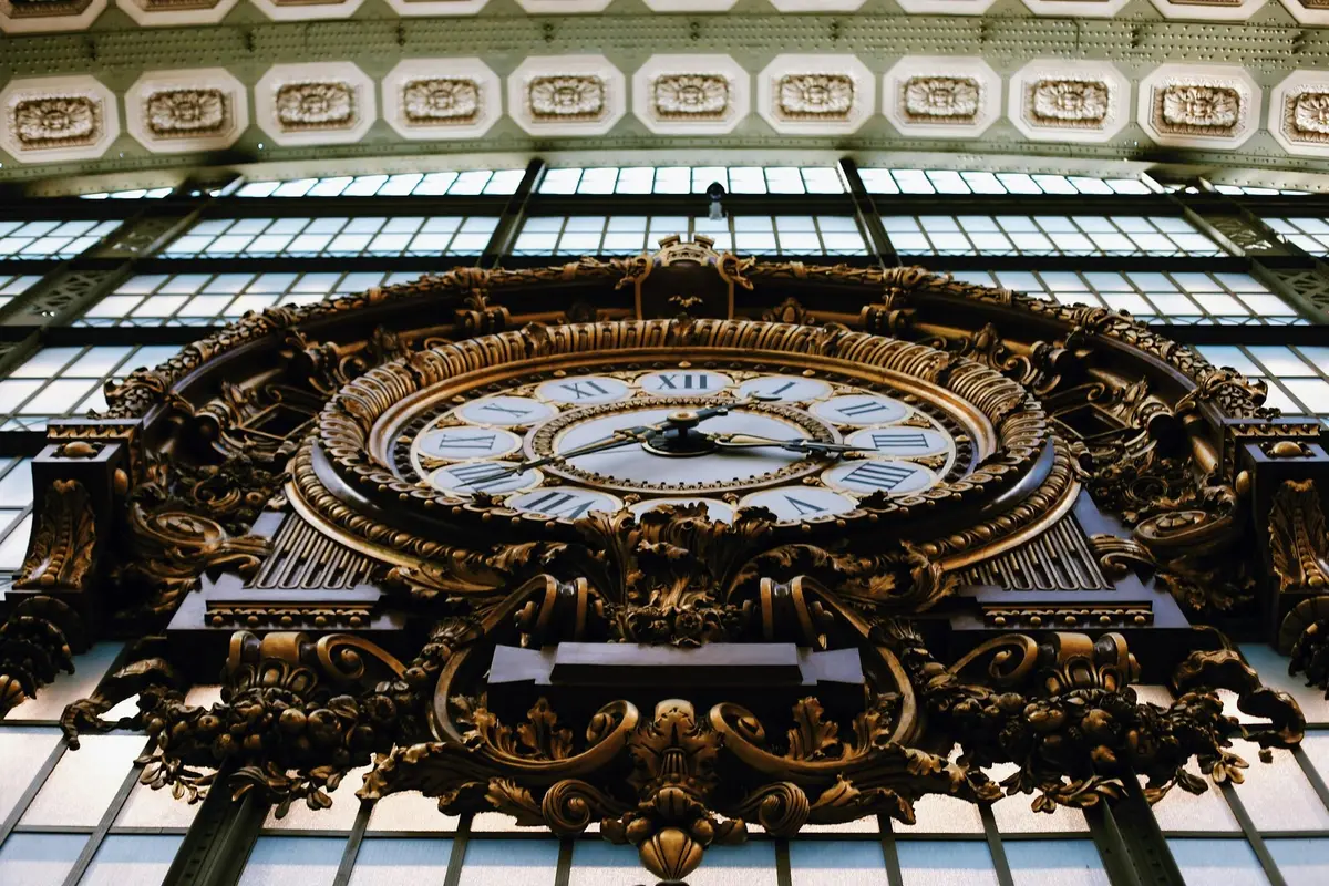 Horloge antique ornée de chiffres romains placés dans un cadre doré décoratif contre un grand mur vitré.