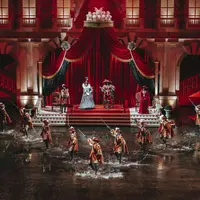 Une représentation théâtrale mettant en scène des acteurs en costumes d'époque sur une scène remplie d'eau avec une toile de fond royale. DR