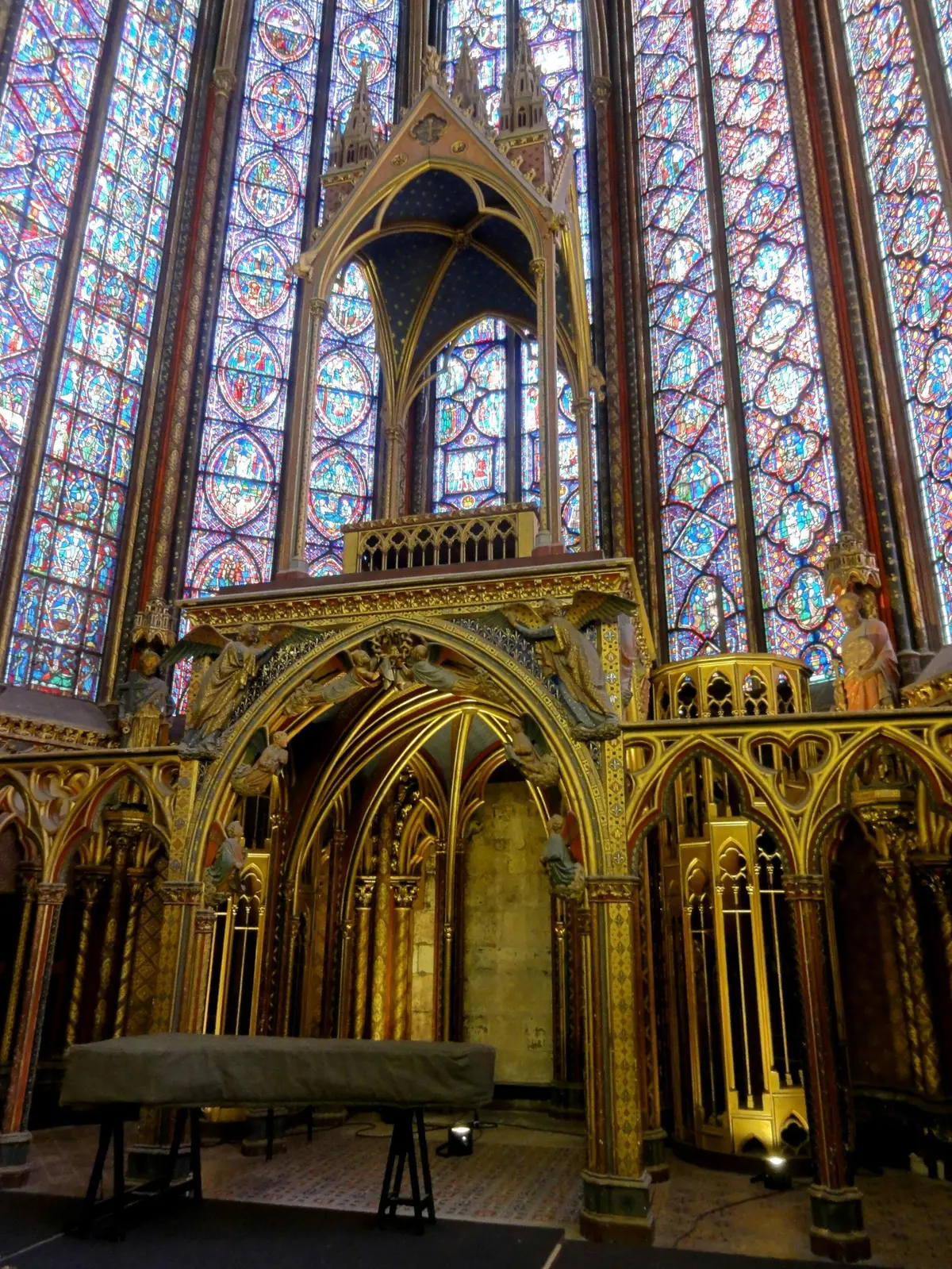 Intérieur gothique complexe avec des arcs ornés et des vitraux colorés, représentant une église ou une cathédrale.