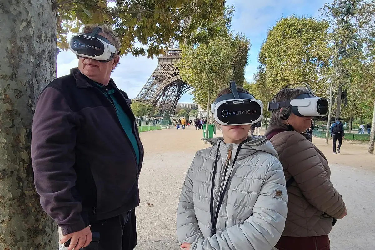 Trois personnes portant des casques de RV se tiennent près de la Tour Eiffel, entourées d'arbres et d'un ciel dégagé.