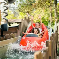 Deux enfants souriants sur un toboggan de bois rouge, les bras levés, alors qu'ils s'éclaboussent dans l'eau. Verdure environnante et clôture en bois. &copy; Walibi Rhone Alpes