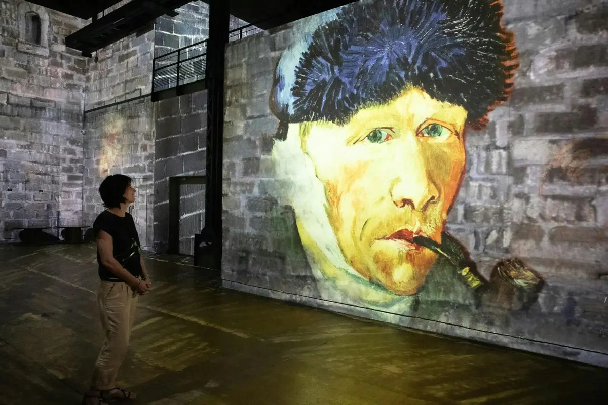 Projection d'un tableau représentant un homme coiffé d'un bonnet de fourrure et tenant une pipe, sur un mur de briques texturé dans un espace intérieur.