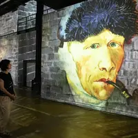 Projection d'un tableau représentant un homme coiffé d'un bonnet de fourrure et tenant une pipe, sur un mur de briques texturé dans un espace intérieur. &copy; Culturespaces___Cyrille_de_la_Motte_Rouge