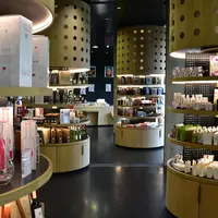 Un intérieur de magasin moderne avec des étagères en bois incurvées et des présentoirs cylindriques, mettant en valeur divers flacons, boîtes et produits. DR