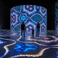 Trois personnes se trouvent dans une pièce sombre éclairée par de grandes projections lumineuses colorées et kaléidoscopiques sur le sol et les murs. &copy; © Cultuirespaces