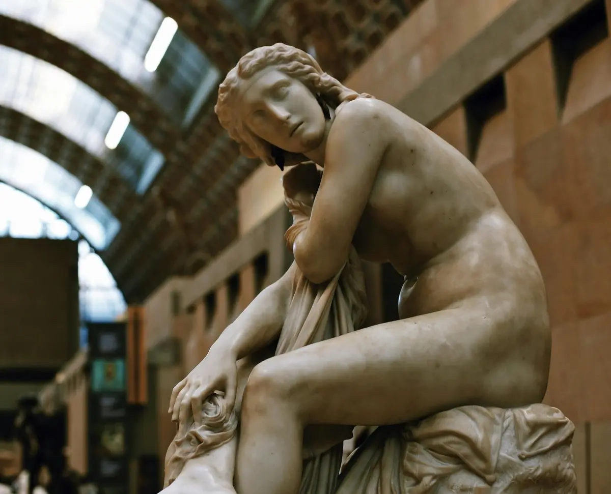 Statue en marbre représentant un personnage assis, drapé, dans une attitude contemplative, dans un musée au plafond voûté et vitré.