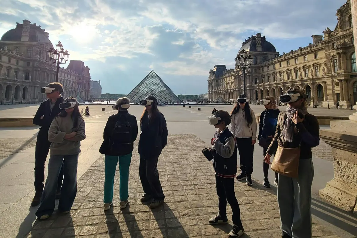 Des personnes portant des casques de réalité virtuelle devant la pyramide du Louvre par une journée ensoleillée.