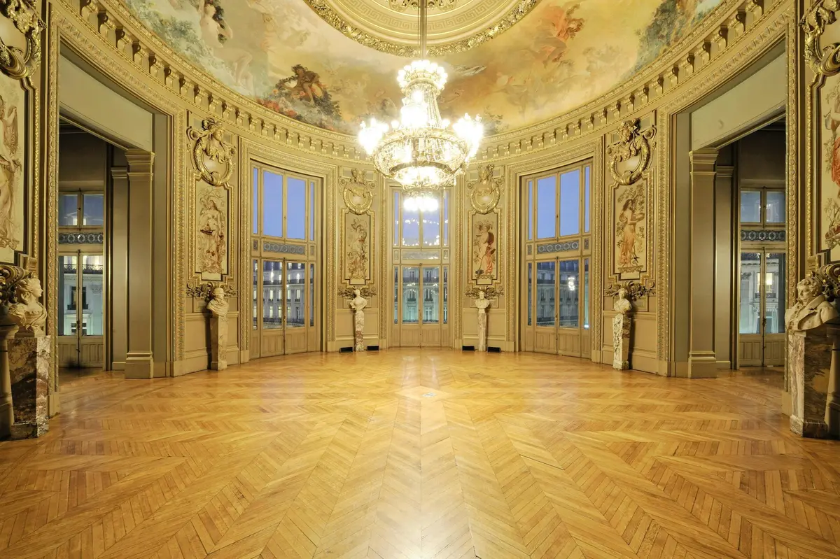 Une pièce circulaire richement décorée, dotée de grandes fenêtres, d'un plafond peint, d'un lustre central et d'un parquet en bois.