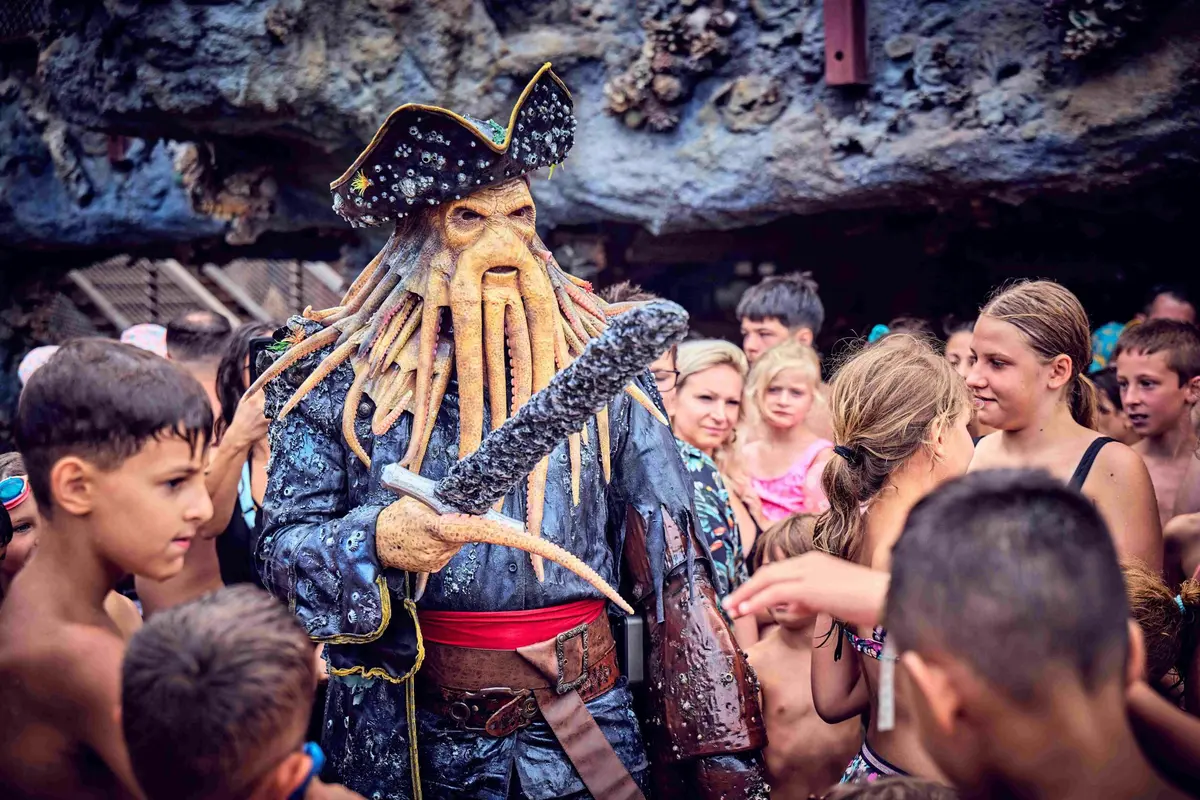 Une personne en costume de pirate avec des tentacules interagit avec un groupe d'enfants dans un environnement extérieur bondé.