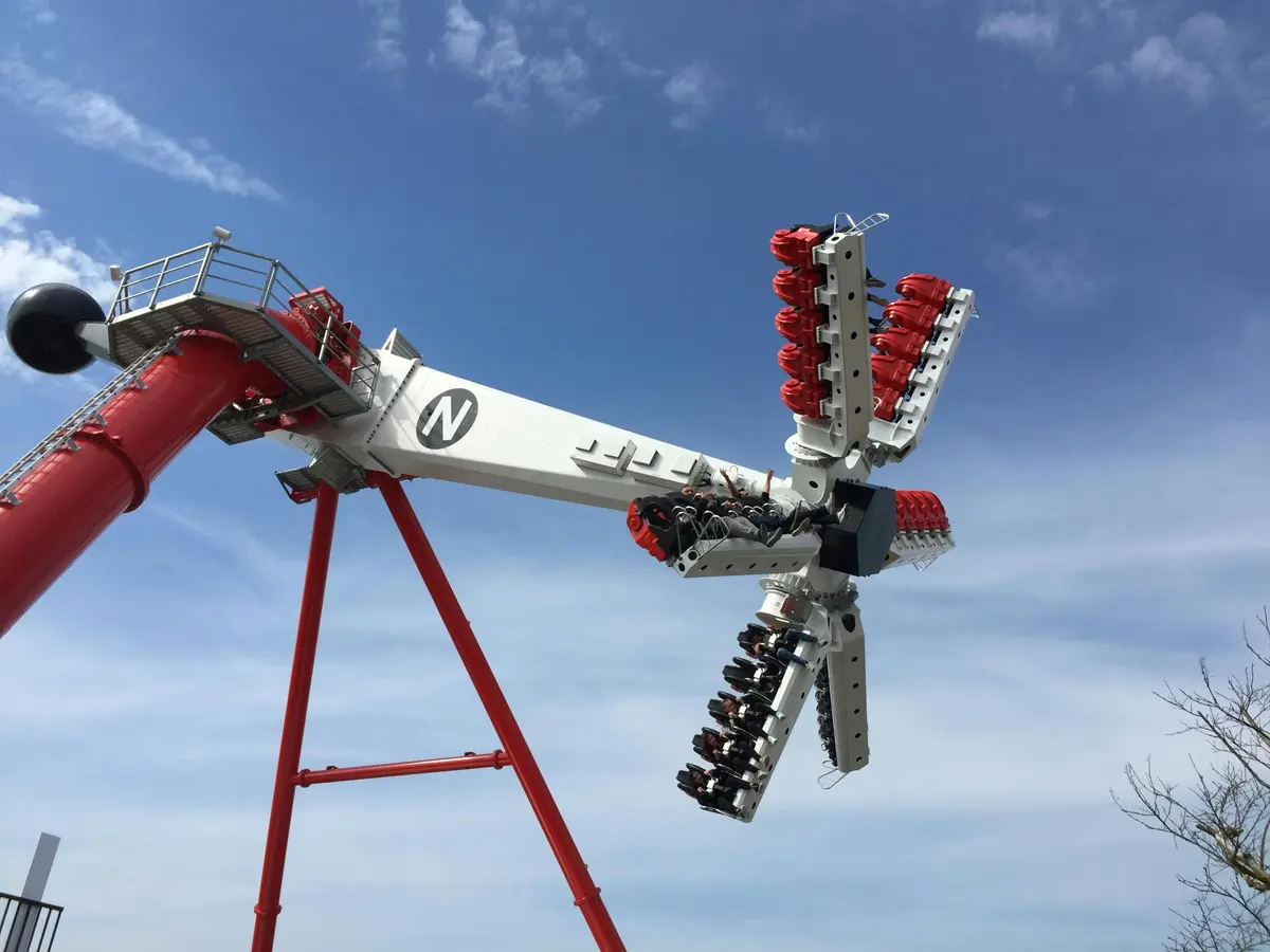 Manège de carnaval avec des bras rotatifs et des sièges rouges, élevant les passagers dans les airs sur fond de ciel bleu et de nuages.