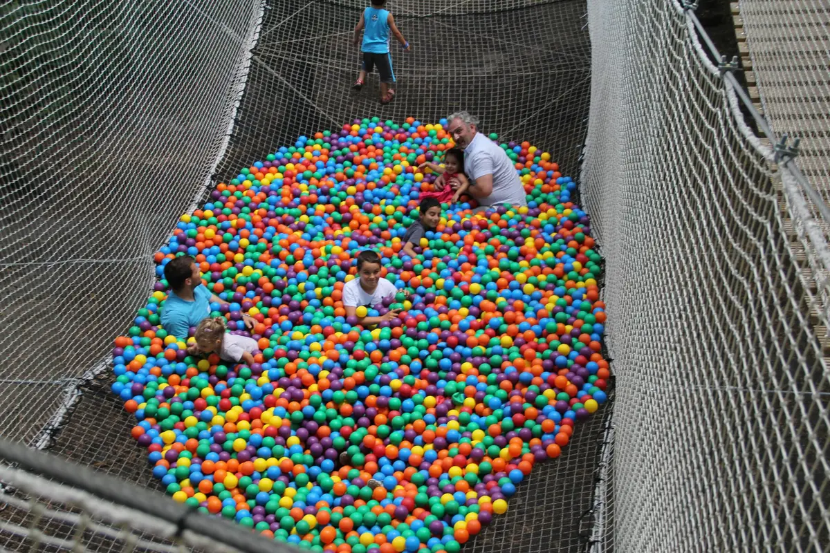 Plusieurs personnes jouent dans un grand terrain de jeu rempli de balles en plastique colorées, entouré de filets de sécurité.