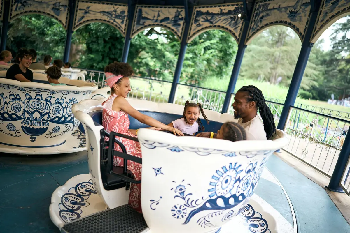 Une famille de quatre personnes fait un tour dans une tasse à thé dans un parc d'attractions. Ils sourient tous et s'accrochent au manège.