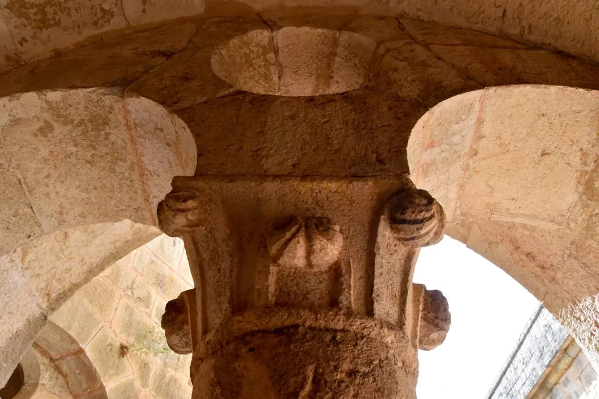 Gros plan d'une ancienne colonne de pierre avec des sculptures détaillées soutenant un arc, mettant en valeur les textures et l'artisanat.