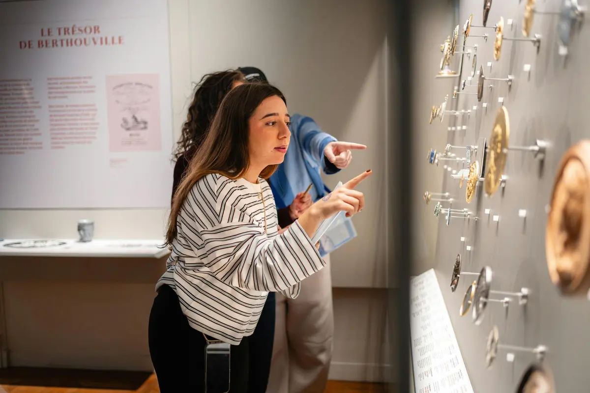Deux personnes dans un musée examinant une exposition de petits objets, l'une d'elles pointant un objet et en discutant avec intérêt.