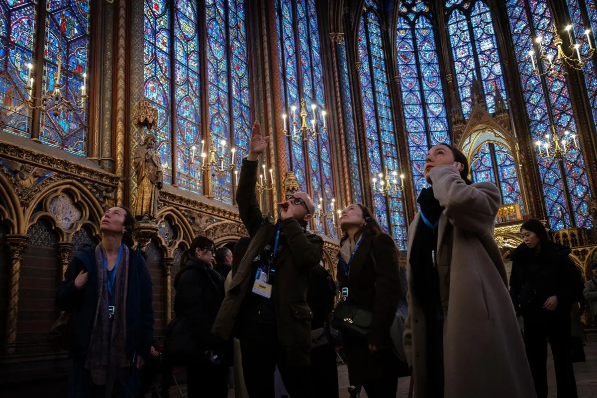 Personnes admirant les vitraux complexes et l'intérieur orné d'une cathédrale historique avec de grands chandeliers.