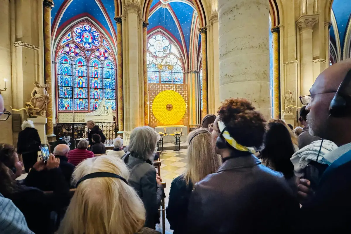 Des personnes se trouvent à l'intérieur d'une cathédrale aux vitraux complexes et à la grande lumière circulaire jaune.