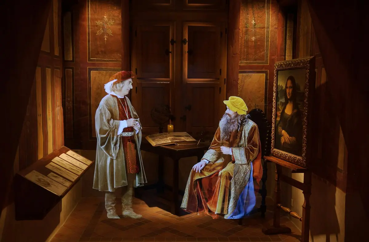 Deux personnages historiques en tenue d'époque dans un bureau avec des armoires en bois, un bureau, de vieilles cartes et un portrait encadré de la Joconde.