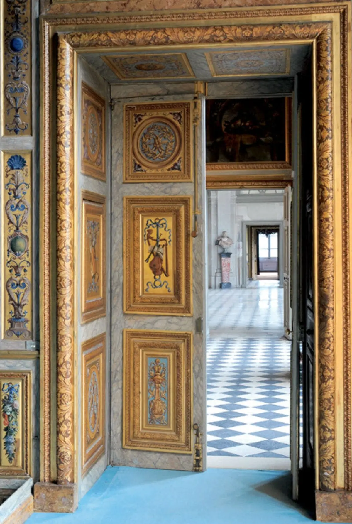 Porte ornée de motifs dorés et colorés complexes, s'ouvrant sur un hall au sol carrelé et orné de statues classiques.