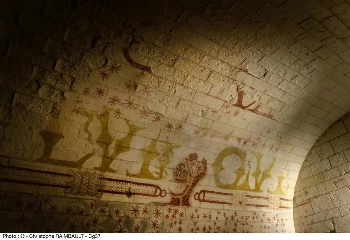 Un vieux mur de briques avec des motifs peints en rouge et jaune délavés, y compris des étoiles et des formes abstraites. Le texte du bas indique RAIMBAULT - Cg37.