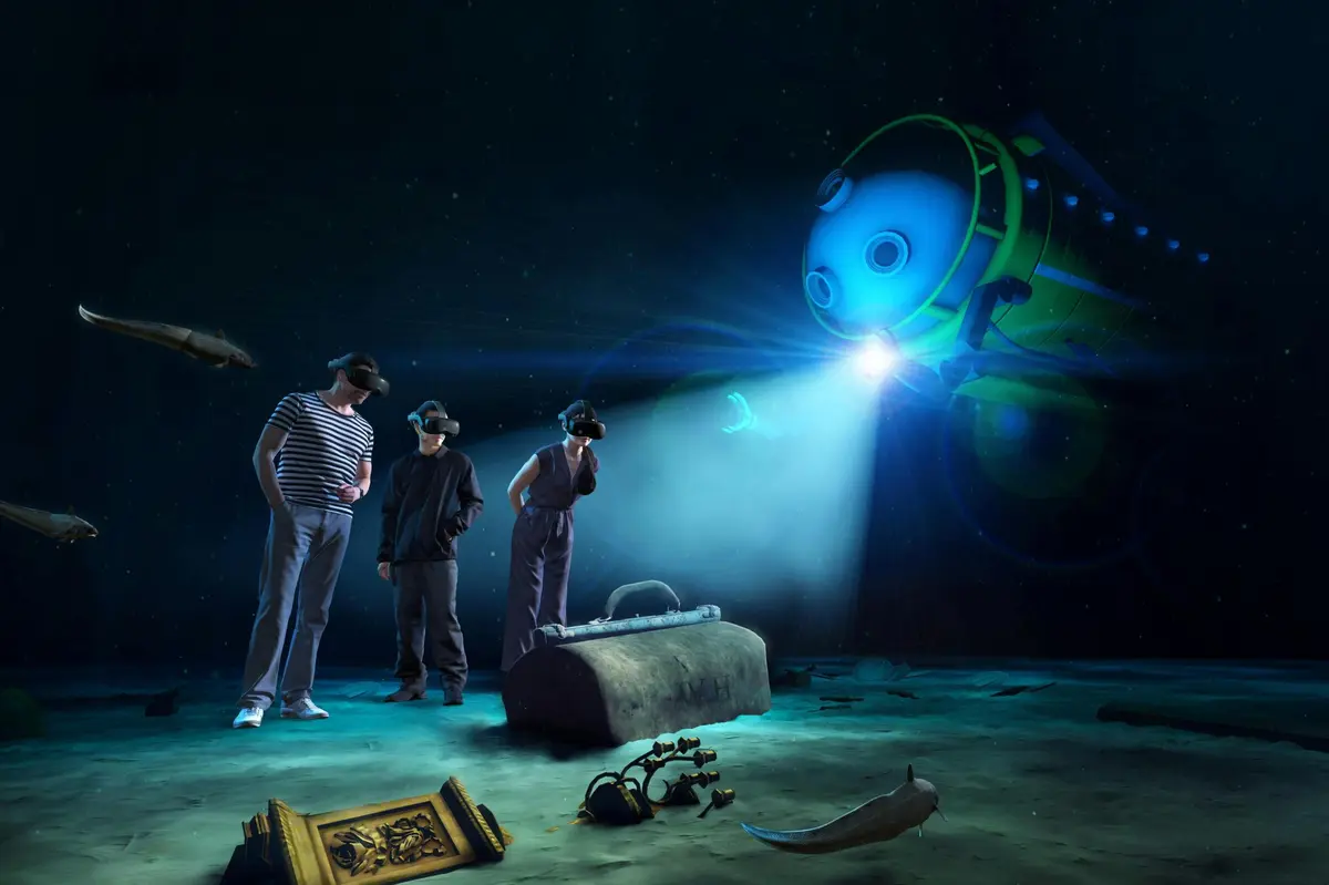 Trois personnes portant des casques de RV se tiennent sur une scène sous-marine simulée avec une épave, un coffre au trésor et un submersible.