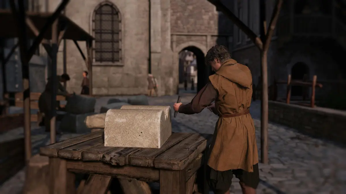 Une personne en tenue médiévale cisèle un bloc de pierre sur une table en bois dans une rue pavée avec des bâtiments en pierre à l'arrière-plan.