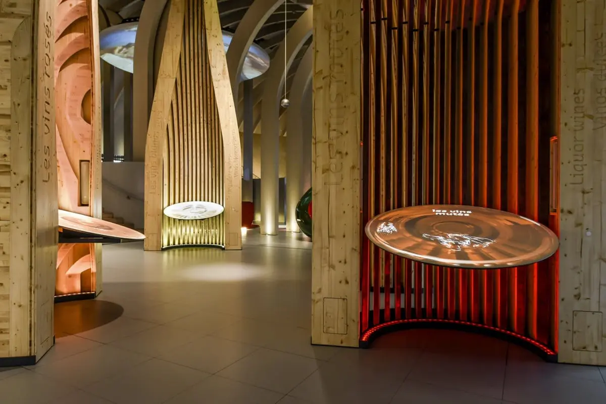 Une exposition muséale moderne avec des structures en bois et des présentations circulaires éclairées dans une pièce faiblement éclairée.