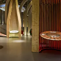 Une exposition muséale moderne avec des structures en bois et des présentations circulaires éclairées dans une pièce faiblement éclairée. DR