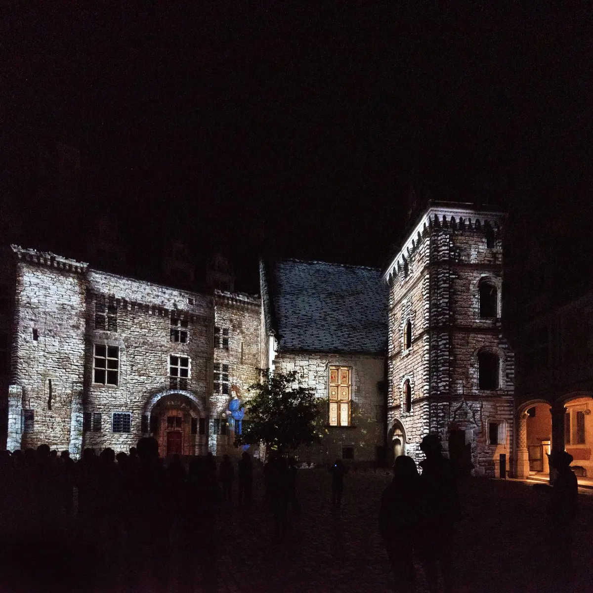 Bâtiments historiques illuminés de nuit avec divers détails architecturaux et un groupe de personnes au premier plan.