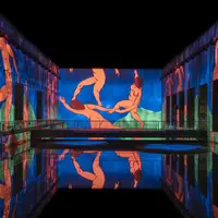 Projection colorée de personnages sur les murs entourant un bassin réfléchissant dans un espace sombre. &copy; @Culturespaces / Geoffroy Groult