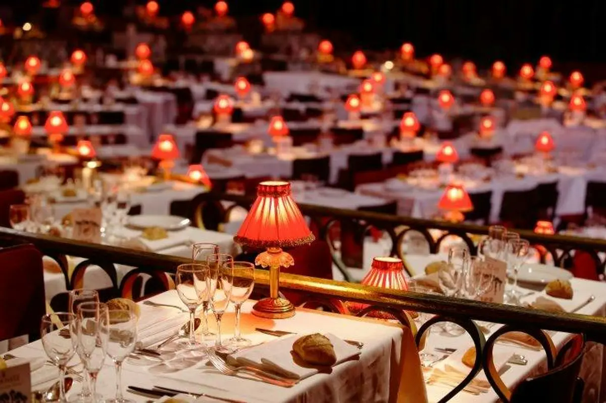 Un restaurant où les tables sont dressées avec des nappes blanches, des lampes rouges, de la verrerie et du pain, créant ainsi une ambiance chaleureuse et élégante.