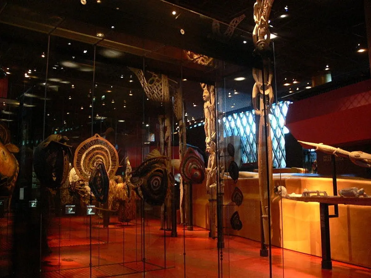 Exposition muséale présentant divers masques et objets tribaux exposés dans des vitrines sous un éclairage tamisé.