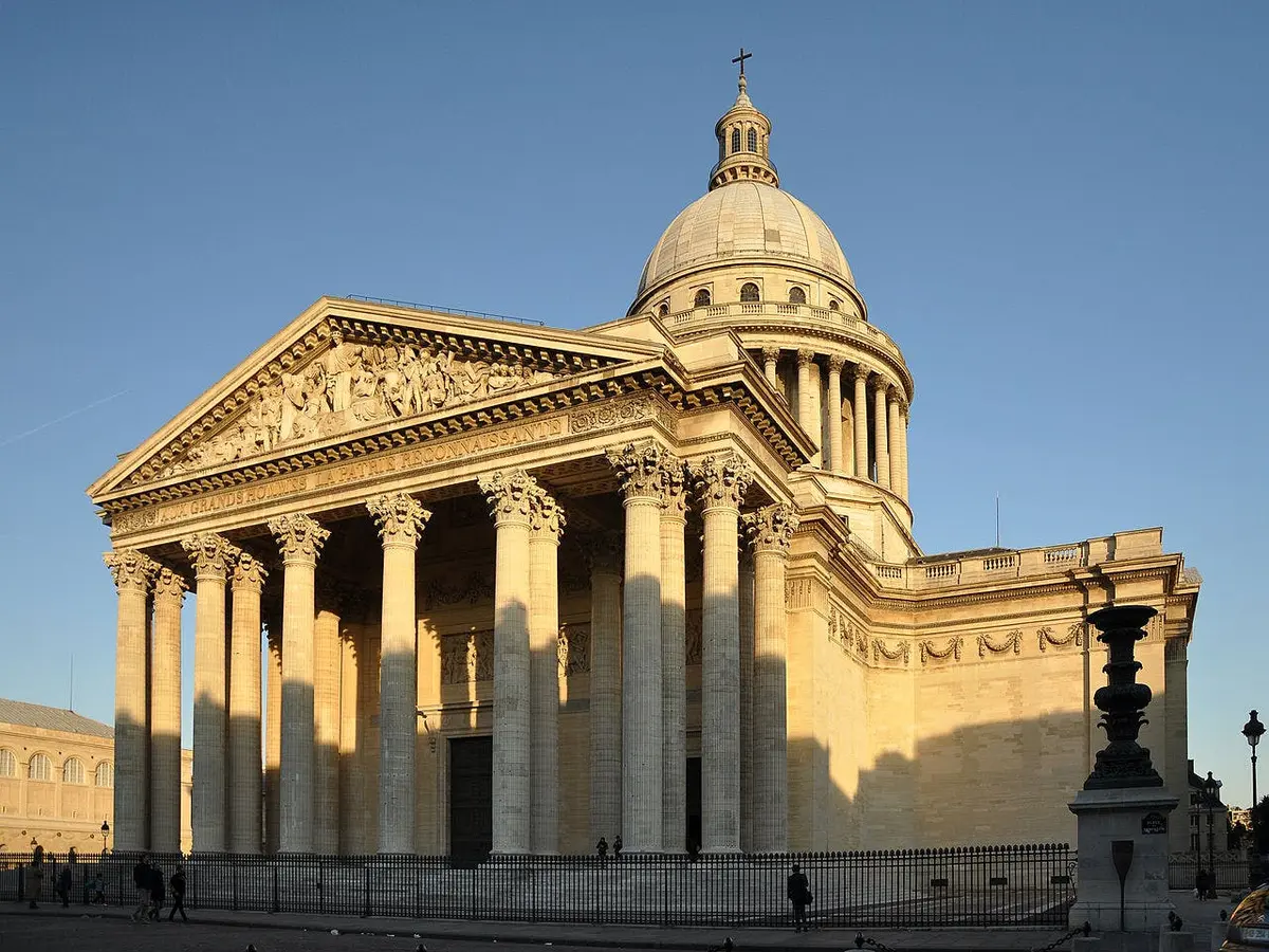 Bâtiment néoclassique avec un grand dôme, des colonnes corinthiennes et des frontons sculptés, le tout sur fond de ciel clair.