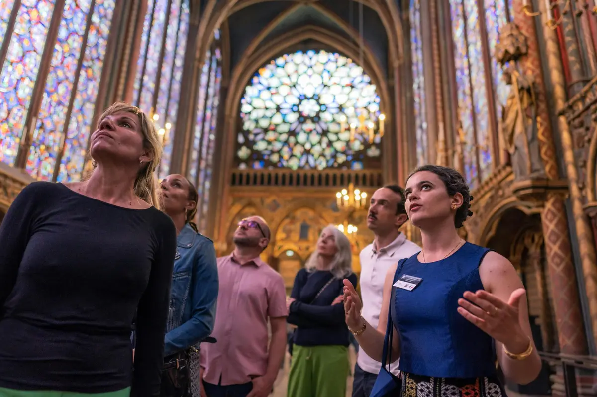 Des personnes se trouvent à l'intérieur d'une cathédrale aux vitraux, écoutant un guide qui parle en faisant des gestes.
